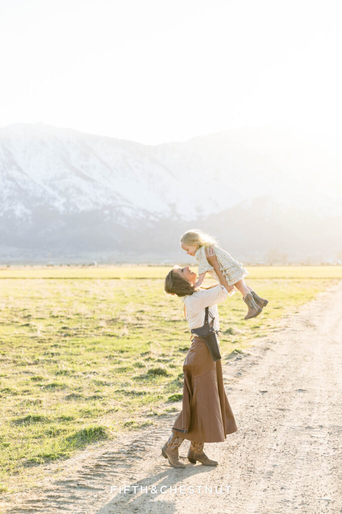 A mother holding her daughter in the air at Gansberg Ranch for western themed family portraits in Gardnerville