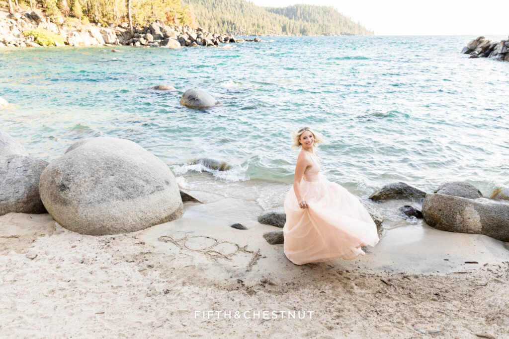 Senior girl twirls in her flowy ball gown with her graduating class written the sand to celebrate her senior year at Lake Tahoe.