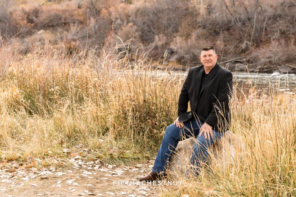 Classic fall outdoor headshots by Reno Headshot Photographer at Mayberry Park of man wearing a black jacket, a black button-up, jeans and cowboy boots by the river.