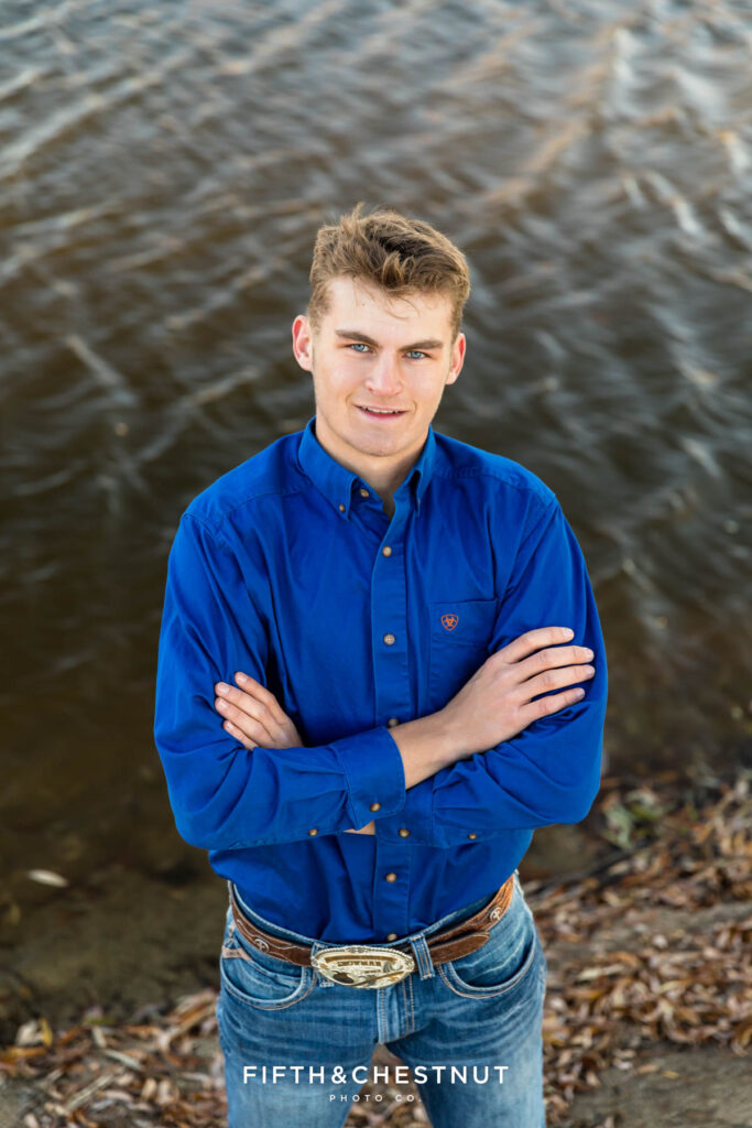 Portrait of a Loyalton High School senior from above with a Sierra Valley pond in the background behind him as he wears a royal blue long-sleeve button-up shirt with jeans.