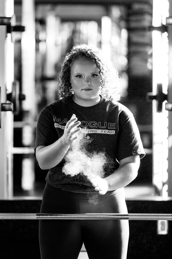 Manogue High School Senior clapping chalk off her hands before lifting weights as a Manogue weightlifter for a portrait by Reno Senior Photographer
