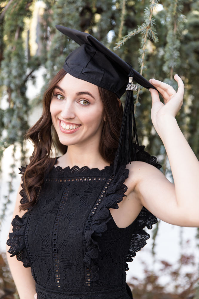 A beautiful UNR grad shows off her cap while wearing a stunning black dress for her college grad portraits at UNR by Reno Grad Photographer.