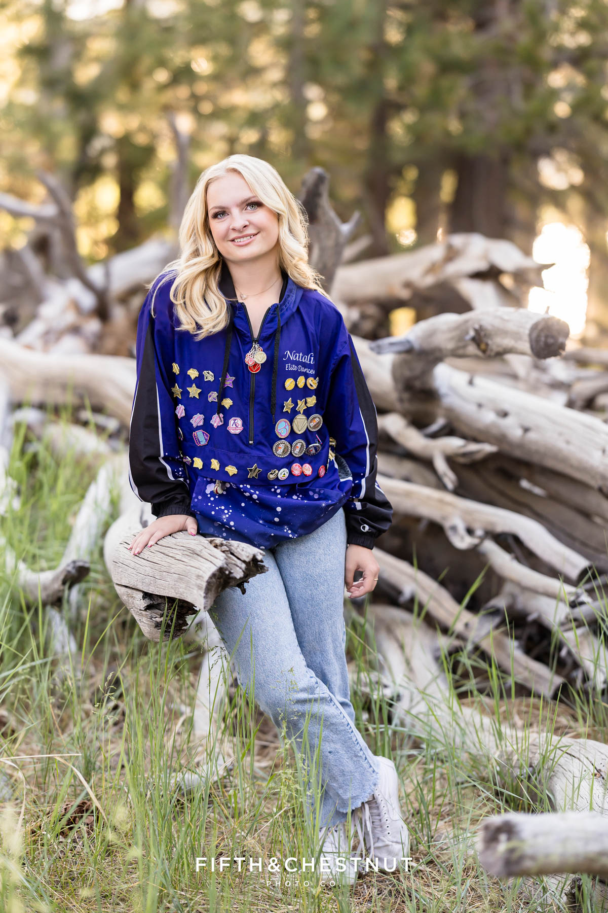 Reno High School Senior smiling in her Art in Motion jacket with forest background