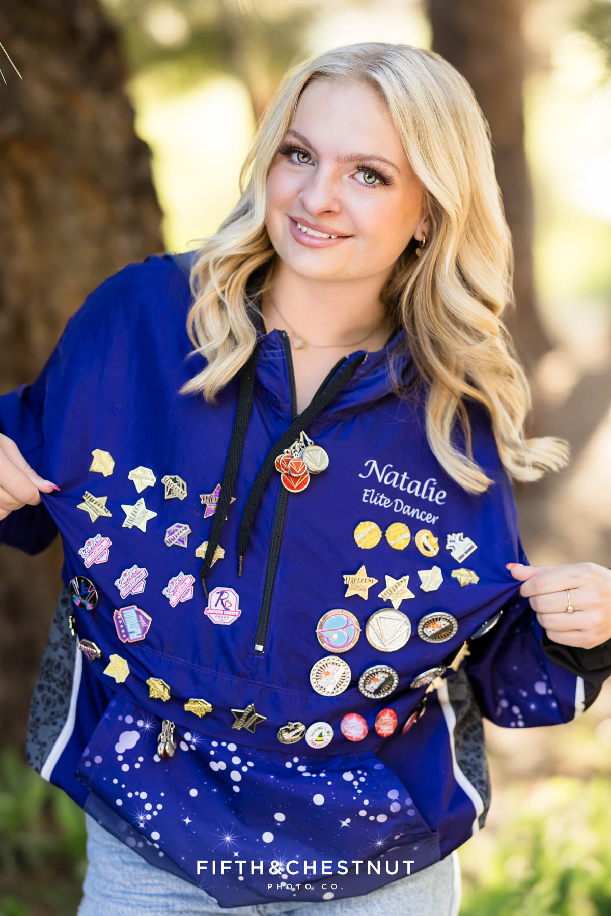Reno High School Senior smiling in her Art in Motion jacket with forest background