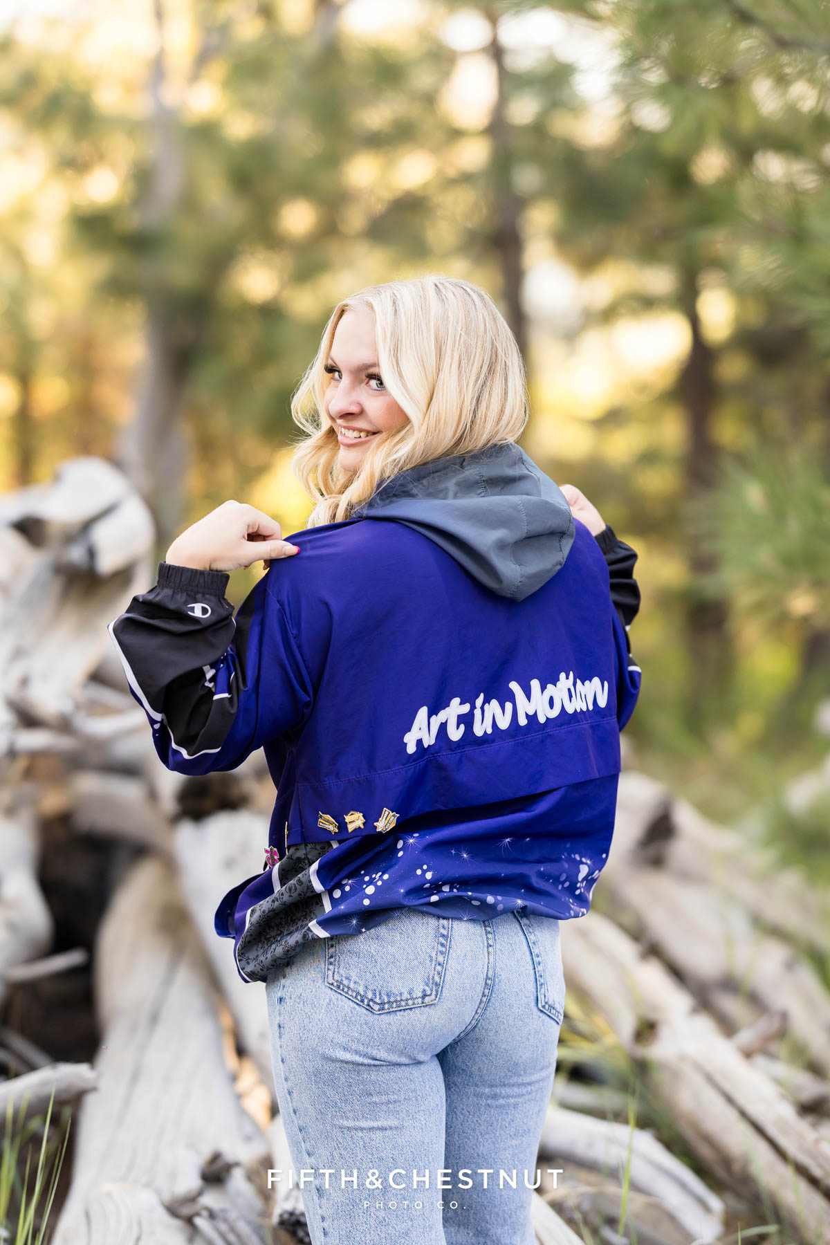 Reno High School Senior smiling in her Art in Motion jacket with forest background