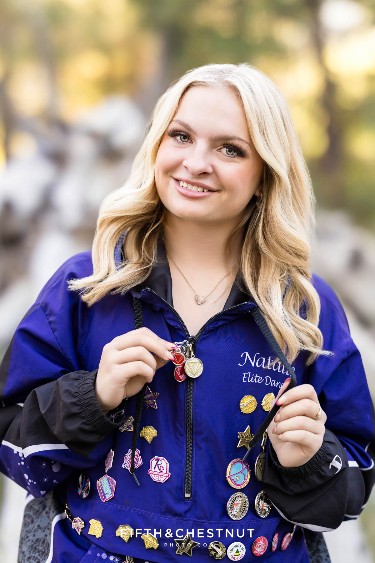 Reno High School Senior smiling in her Art in Motion jacket with forest background
