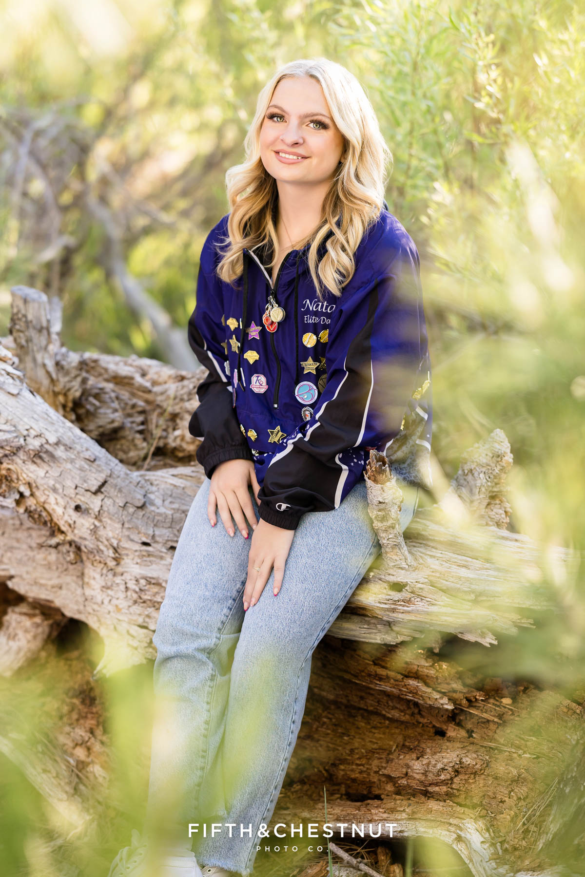 Reno High School Senior smiling in her Art in Motion jacket with forest background