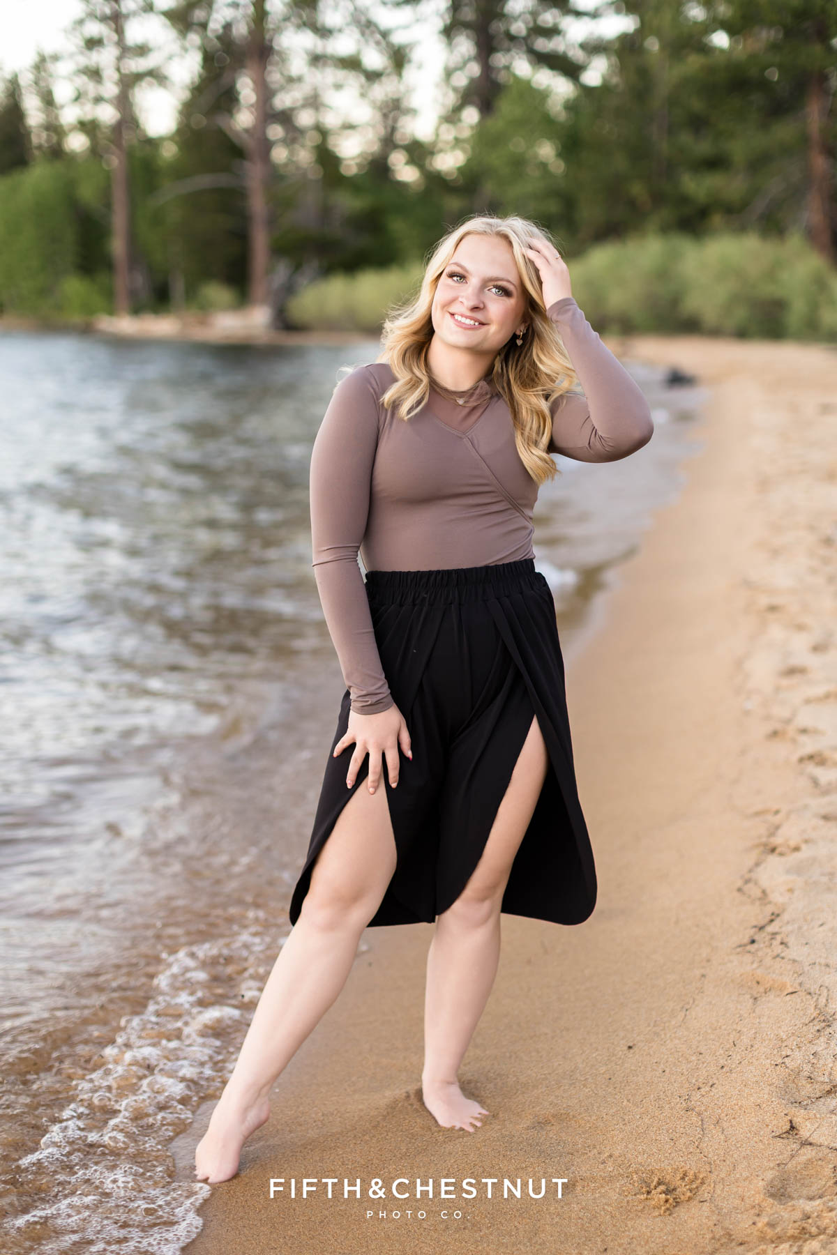 Reno High School Senior smiling on the shore in the waves with mountain and forest  backdrop in South Lake Tahoe