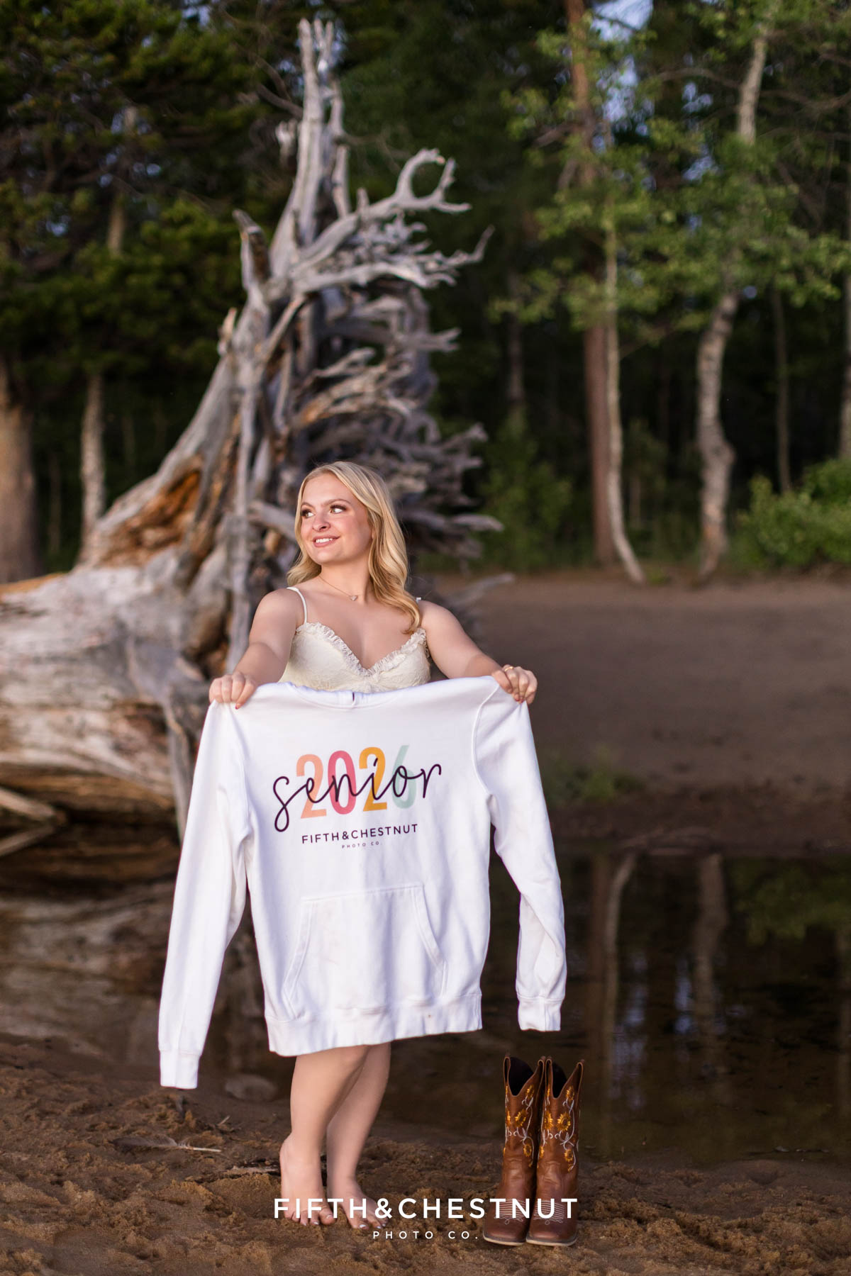Reno High School Senior holding her “Senior 2026” sweatshirt with boots beside her on the beach
