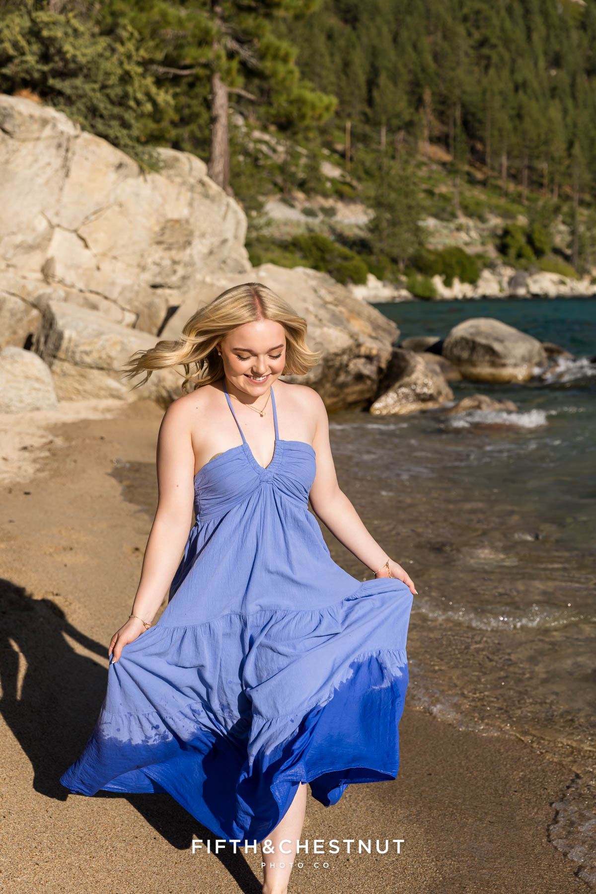 Reno High School senior running down the beach in lake tahoe as the sun shines on her in a long blue maxi dress.