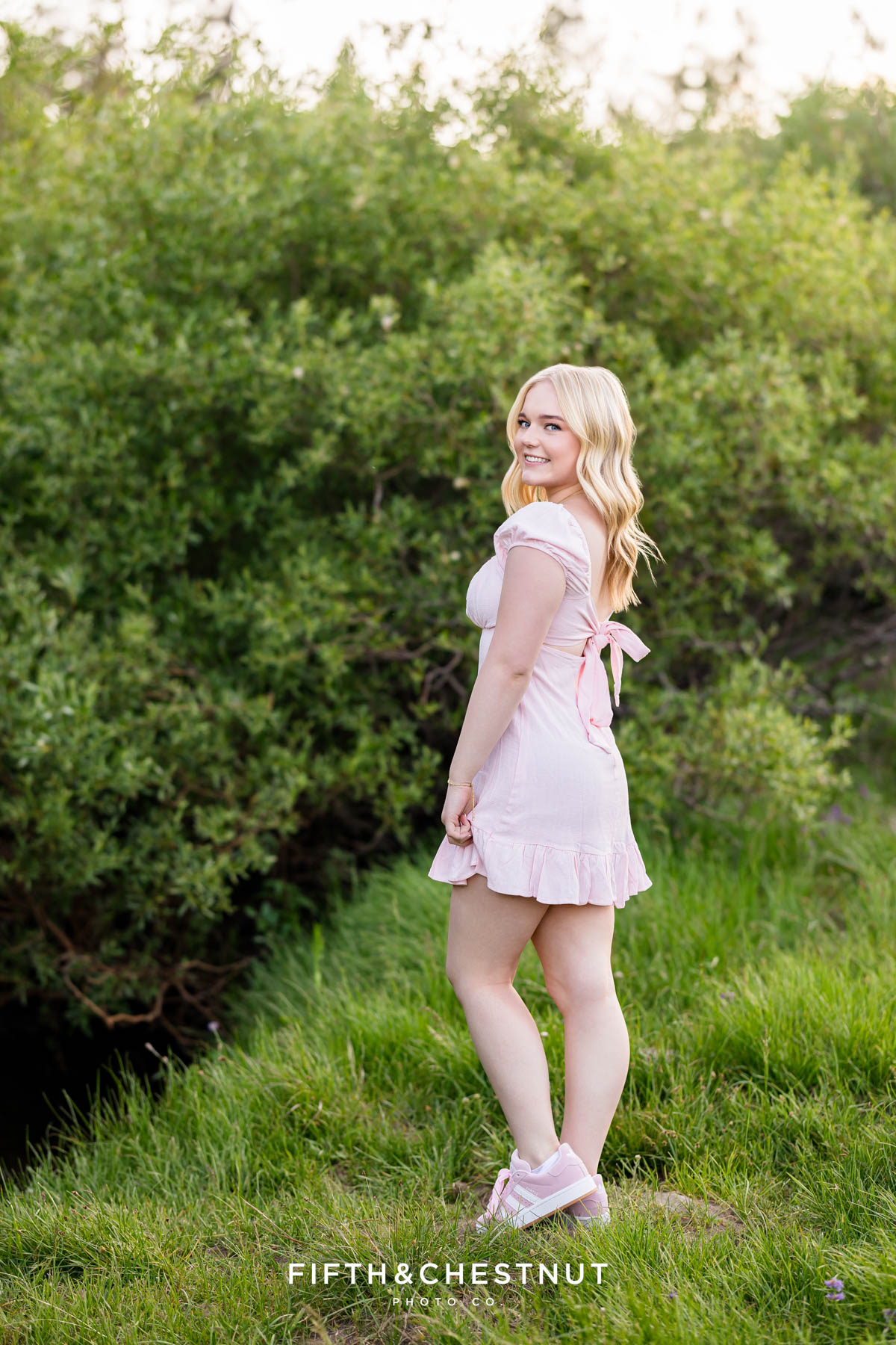 Bishop Manogue Senior smiling in a pink dress on a lush green hillside in the Tahoe Meadows