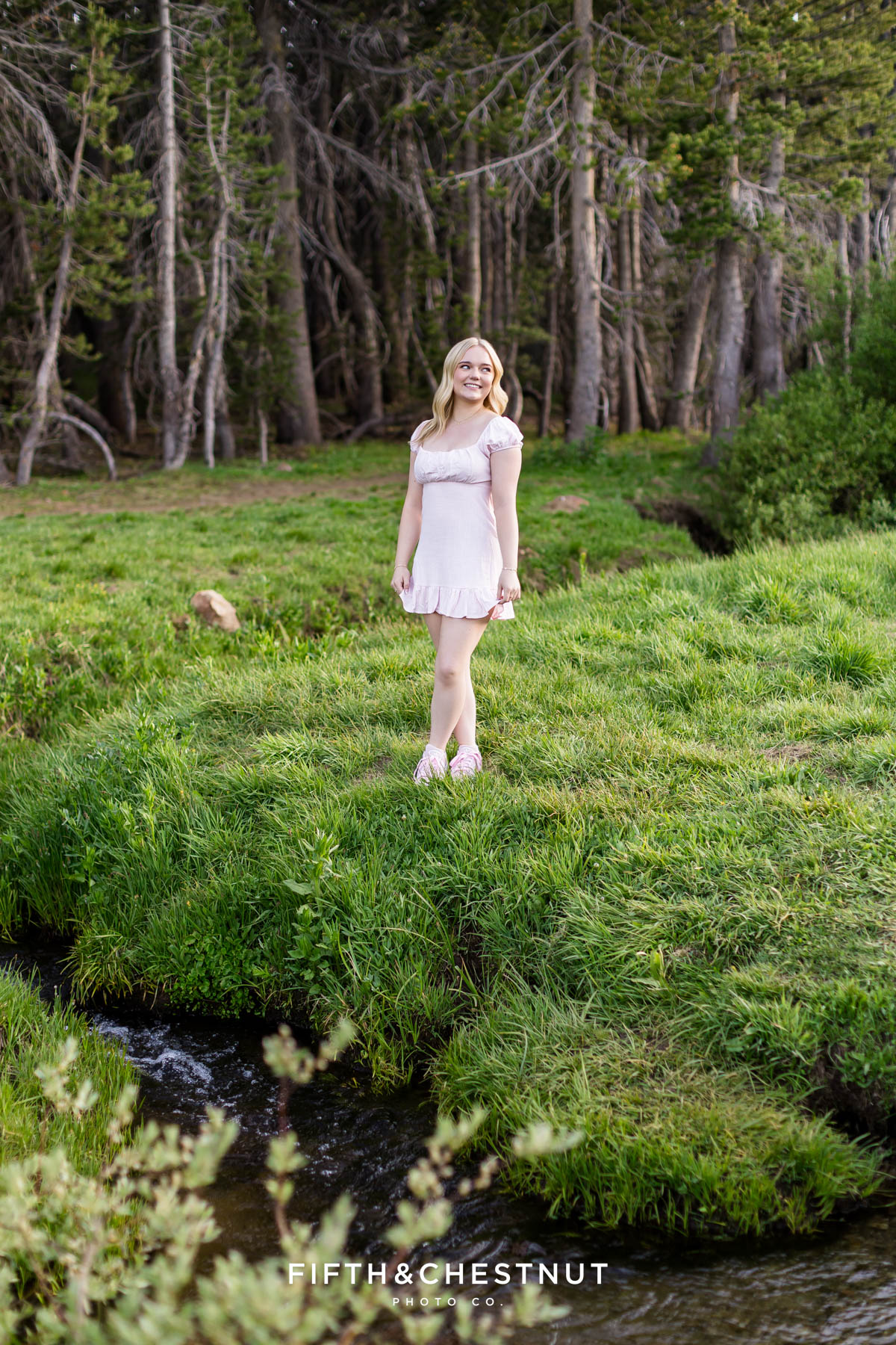 Bishop Manogue Senior smiling in a pink dress on a lush green hillside in the Tahoe Meadows
