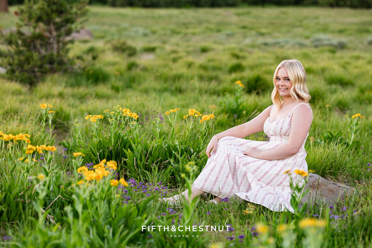 Bishop Manogue Senior sitting in a wildflower-filled meadow with a lush forest background